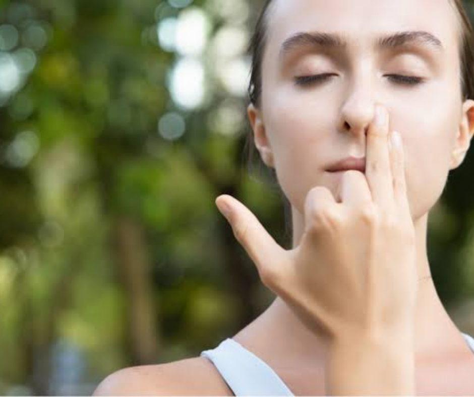 A woman outdoors with eyes closed, fingers raised to her nose in the alternate nostril breathing position of Anulom Viloma